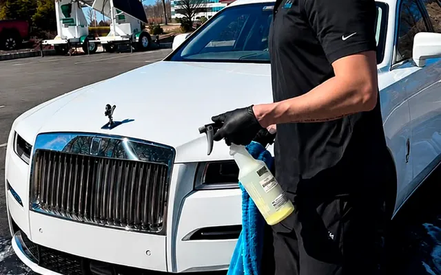 Andrew detailing a white Rolls-Royce with a spray bottle and microfiber towel